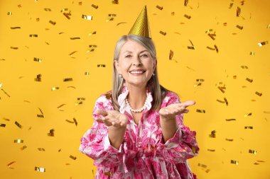 Mutlu yaşlı kadın ve sarı arka planda uçan konfeti