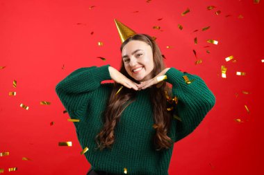 Kırmızı arka planda parti şapkası takan mutlu genç bir kadın.