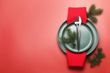 Kırmızı arka planda tabaklar, çatal bıçaklar ve köknar dalları olan bir Noel ortamı. Metin için boşluk