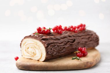 Lezzetli Noel kütüğü (geleneksel Noel pastası) kırmızı üzümlü masada bulanık ışıklara karşı, yakın plan. Bokeh etkisi