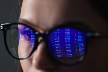 Gri arka planda yansıması olan gözlük takan genç bir kadın, yakın plan.