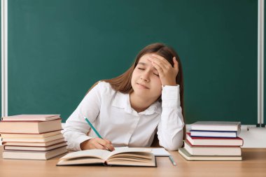 Okula dönelim. Öğrenci ahşap masada karatahtaya karşı çalışıyor.