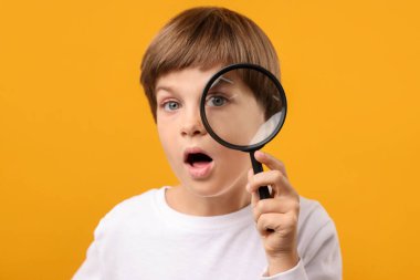 Sarı arka planda büyüteç olan küçük çocuk şaşırdı.