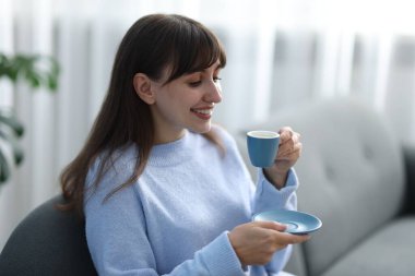 Evdeki kanepede kahve molası veren gülümseyen kadın.