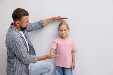 Babası küçük kızının boyunu ölçüyor. Kapalı alanda bir duvarın yanında..