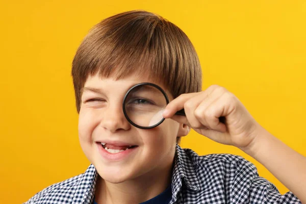 Sarı arka planda büyüteç olan küçük çocuk.