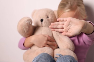 Oyuncak ayılı küçük kız, beyaz duvarın yanında hareketsiz duruyor, seçici odaklı.