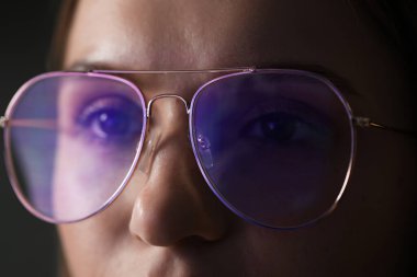 Siyah arka planda gözlük takan genç bir kadın, yakın plan.