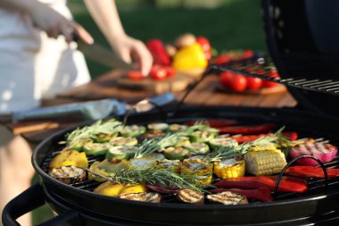 Vejetaryen barbeküsü. Dışarıdaki masada ürünleri kesen kadın, pişmiş sebzelerle ızgaraya odaklan.