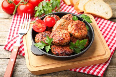 Maydanozlu lezzetli köfteler, tavada domates, ahşap masada çatal, yakın plan.