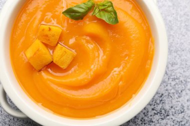 Gri masada servis edilen fesleğenli balkabağı kremalı çorba.