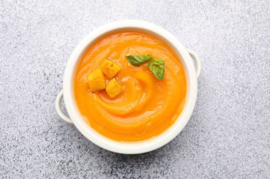 Gri masada servis edilen fesleğenli balkabağı kremalı çorba.