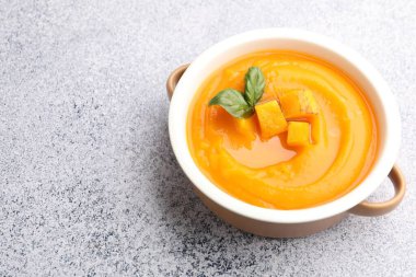 Gri masada servis edilen fesleğenli balkabağı kremalı çorba, yakın plan. Metin için boşluk