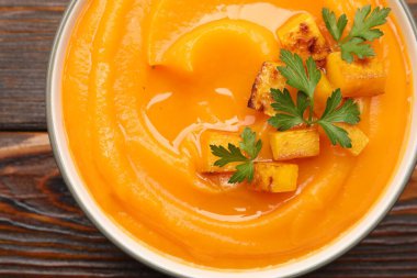 Ahşap masada sunulan maydanozlu lezzetli balkabağı kremalı çorba.