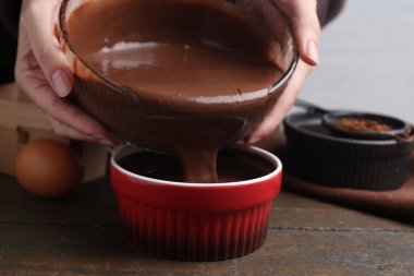 Kadın, ahşap masadaki yemek kabına çikolata hamuru döküyor, yakın plan.