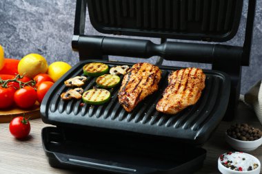 Lezzetli tavuk filetosu, mantar, ürün ve baharat ile elektrikli ızgara ahşap masa üzerinde Gri arka plan, yakın çekim