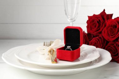 Romantik bir ortam. Nişan yüzüğü, tabak, çatal bıçak takımı ve güller beyaz mermer masada, yakın plan.