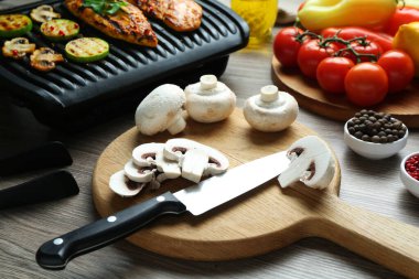 Çiğ mantar, bıçak, tavuk filetosu ve sebzeli ızgara, ahşap masa, yakın plan.