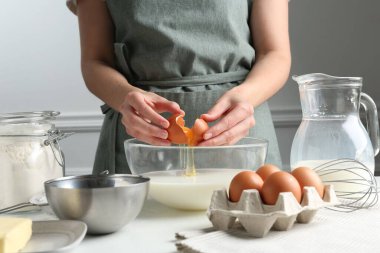 Hamur yapmak (sıvı hamur). Beyaz masadaki kaseye yumurta ekleyen kadın, yakın plan.