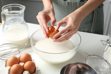 Hamur yapmak (sıvı hamur). Beyaz masadaki kaseye yumurta ekleyen kadın, yakın plan.