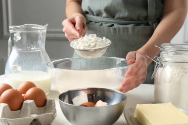 Hamur yapmak (sıvı hamur). Beyaz masada un yiyen bir kadın. Kapalı alanda, yakın plan.