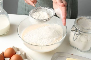 Hamur yapmak (sıvı hamur). Beyaz masada un yiyen bir kadın. Kapalı alanda, yakın plan.