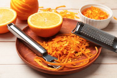 Portakal tadı, taze meyveler, hafif ahşap masada zester aleti ve rende, yakın plan.