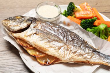 Lezzetli ızgara balık, sebze ve sos ahşap masada, yakın plan.