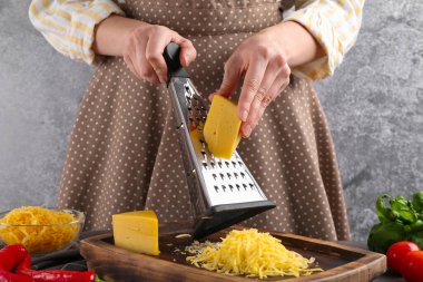 Gri masada peynir rendeleyen kadın, yakın plan.