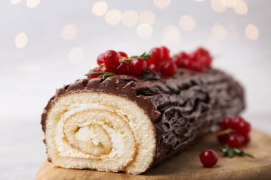 Lezzetli Noel kütüğü (geleneksel Noel pastası) kırmızı üzümlü masada bulanık ışıklara karşı, yakın plan. Bokeh etkisi