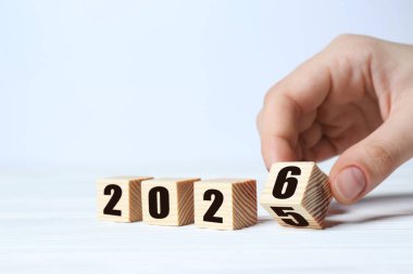 Yeni yıl. Beyaz arkaplanda 2026 yapmak için 5 ve 6 numaralı küpü çeviren kadın, yakın plan