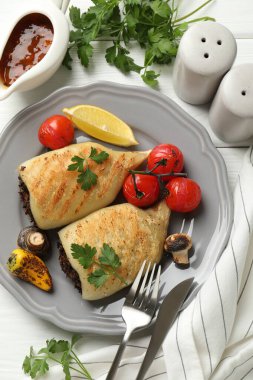 Beyaz ahşap masada servis edilen mantar, maydanoz ve sebzelerle doldurulmuş lezzetli ızgara kalamar parçaları.