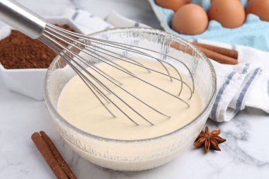 Sıvı hamur kasede, çırpma ve malzemeler beyaz masada, yakın plan.