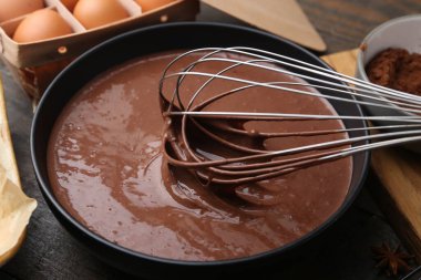 Sıvı çikolata hamurunu ahşap masada çırpma kabıyla karıştırmak, yakın plan.