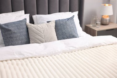 Çarşaflı yatak, komodin, lamba ve su yatak odasındaki gri duvarın yanında.