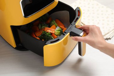 Beyaz ahşap masada ızgara sebzeli fırın açan kadın, yakın plan.