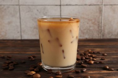 Lezzetli buzlu kahve, bardakta süt, ahşap masada fasulye, fayanslı duvara karşı, yakın plan.