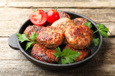 Maydanozlu lezzetli köfteler ve tavada domatesler ahşap masada, yakın plan.