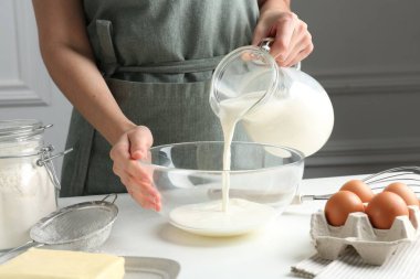 Hamur yapmak (sıvı hamur). Beyaz masadaki kaseye süt döken kadın, yakın plan.