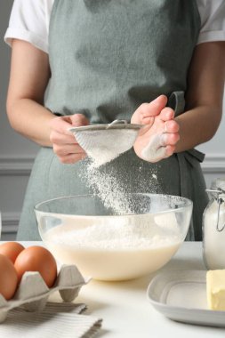 Hamur yapmak (sıvı hamur). Beyaz masada un yiyen bir kadın. Kapalı alanda, yakın plan.
