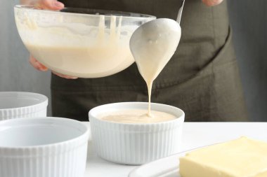 Kadın hamur hamurunu (sıvı hamur) içerideki masada yemek tabaklarına döküyor, yakın plan.