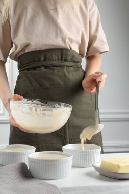 Kadın hamur hamurunu (sıvı hamur) içerideki masada yemek tabaklarına döküyor, yakın plan.