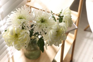 Güzel beyaz kasımpatı çiçekleri vazoda, ahşap rafta.