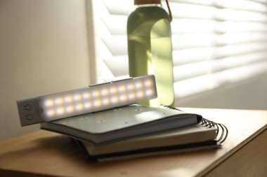 Taşınabilir LED lamba, defterler ve su şişesi komodinin üzerinde, yakın plan.