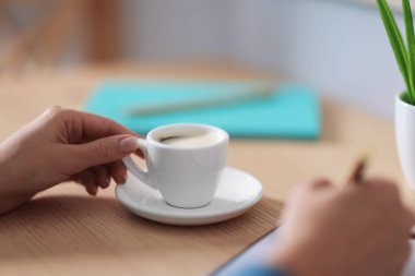 Kahve molası. Ahşap masada fincanla yazan kadın, yakın plan.