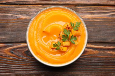 Ahşap masada sunulan maydanozlu lezzetli balkabağı kremalı çorba.