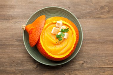 Maydanozlu balkabağı kremalı çorba ve ahşap masada sunulan kızarmış ekmek.