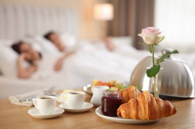 Tahta masada nefis bir kahvaltı ve otel odasında uyuyan çift, seçici bir odak noktası.