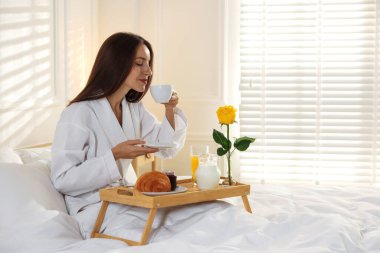 Kadın yatakta nefis kahvaltı yapıyor, mesaj atmak için yer var. Otel oda servisi.