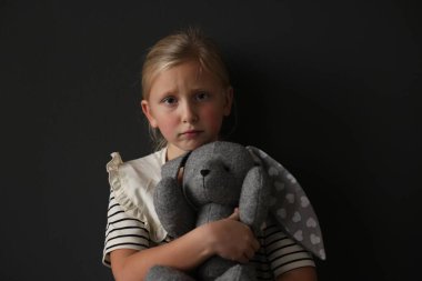 Siyah arka planda oyuncak tavşanı olan üzgün küçük kız.